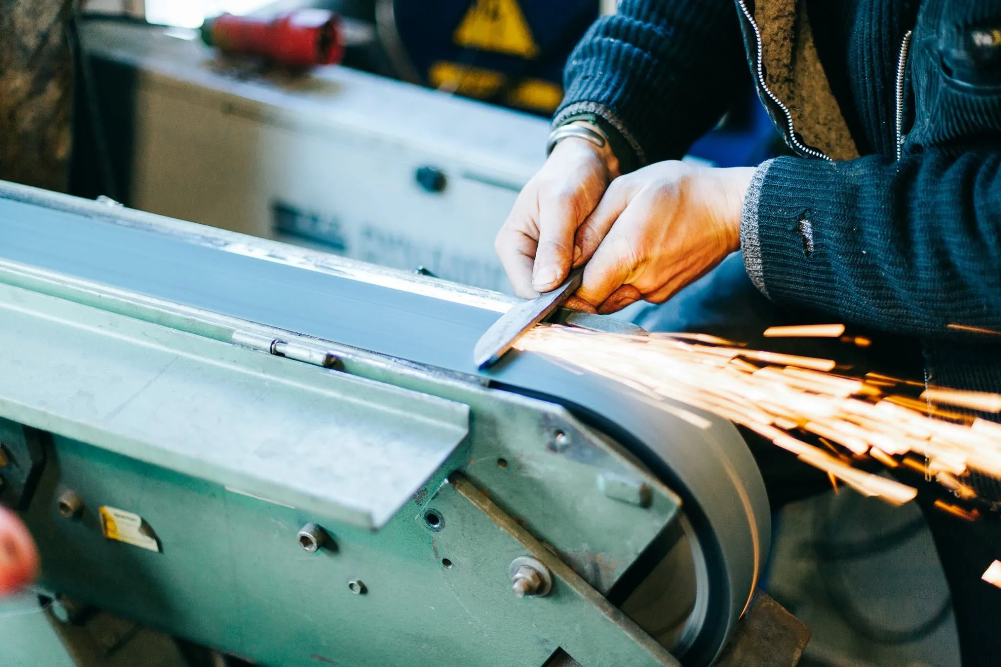 A knie gets ground on a belt grinder, throwing glowing sparks.
