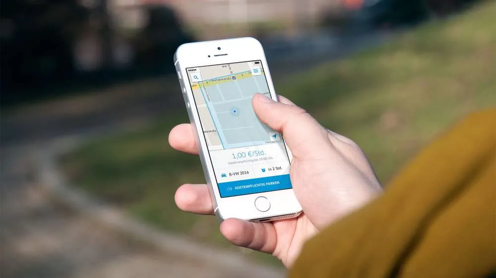 A person holding an older iPhone, app screen shows a map, price per hour and "Start Park Ticket" button.