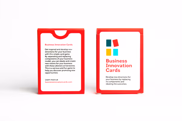 Packaging of the game, a cardboard box with red edges. The front has a logo consisting of 4 colored cards, the game's title 'Business Innovation Cards' and the text 'Develop new directions for your busiess by replacing it's components and ideating the outcomes.'.